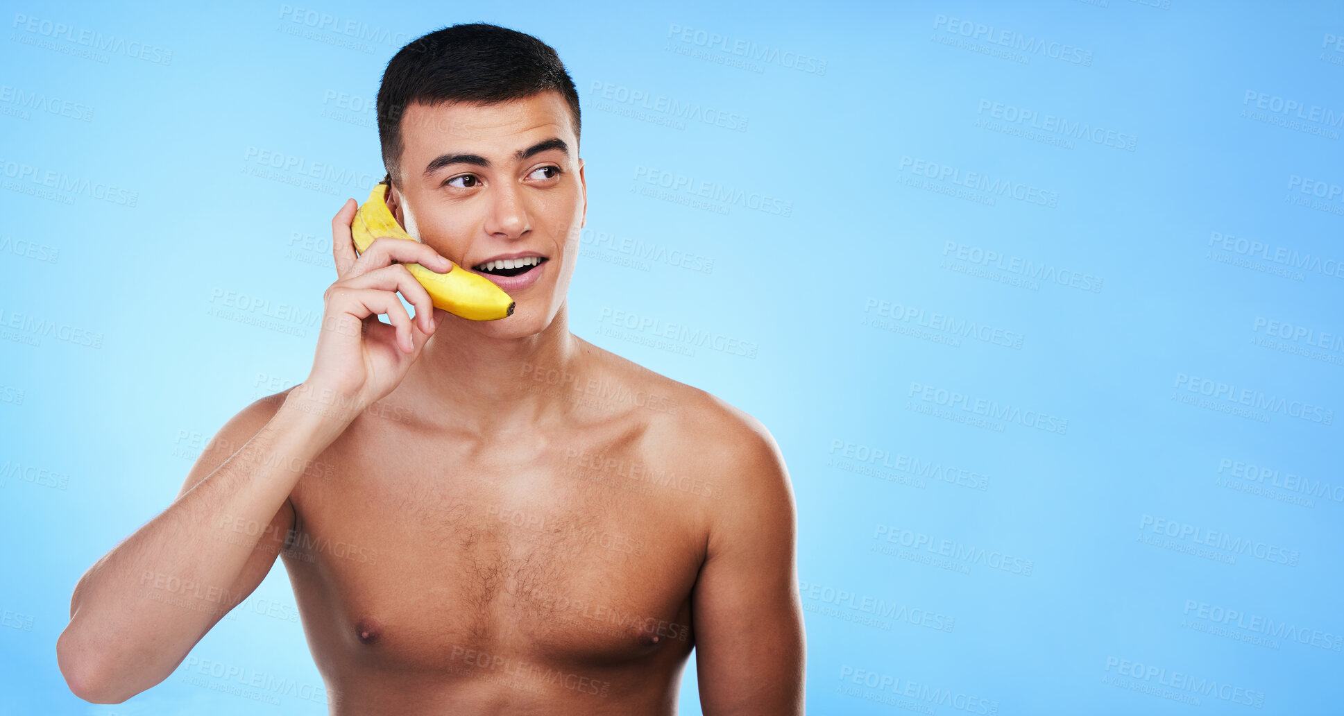 Buy stock photo Phone call, banana and young man in a studio for conversation, gossip or funny discussion. Happy, communication and male model from Canada with fruit cellphone by blue background with mockup space.