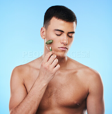 Buy stock photo Man, beauty and face with skin, roller for skincare and grooming with hygiene on blue background. Jade crystal, model and dermatology, cosmetic tools and treatment with facial massage in a studio