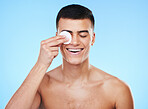 Skincare, beauty and man with cotton pad in a studio for health, wellness and self care routine. Smile, dermatology and young male model with facial cosmetic swab product isolated by blue background.