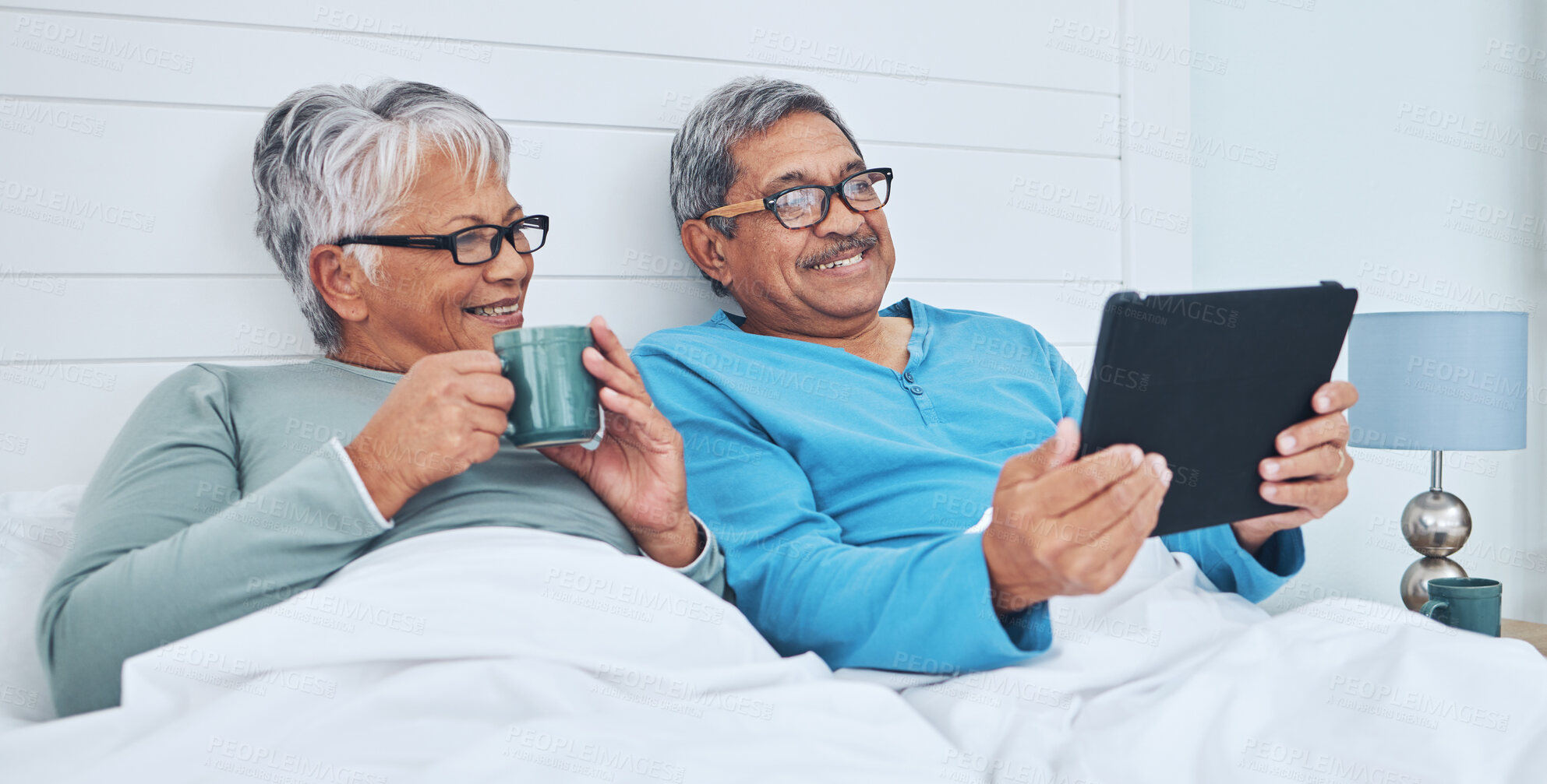 Buy stock photo Tablet, mature couple and coffee in bed at home together on social media, streaming movie and film in the morning. Tech, man and woman drink tea in bedroom, bonding and smile reading news to relax