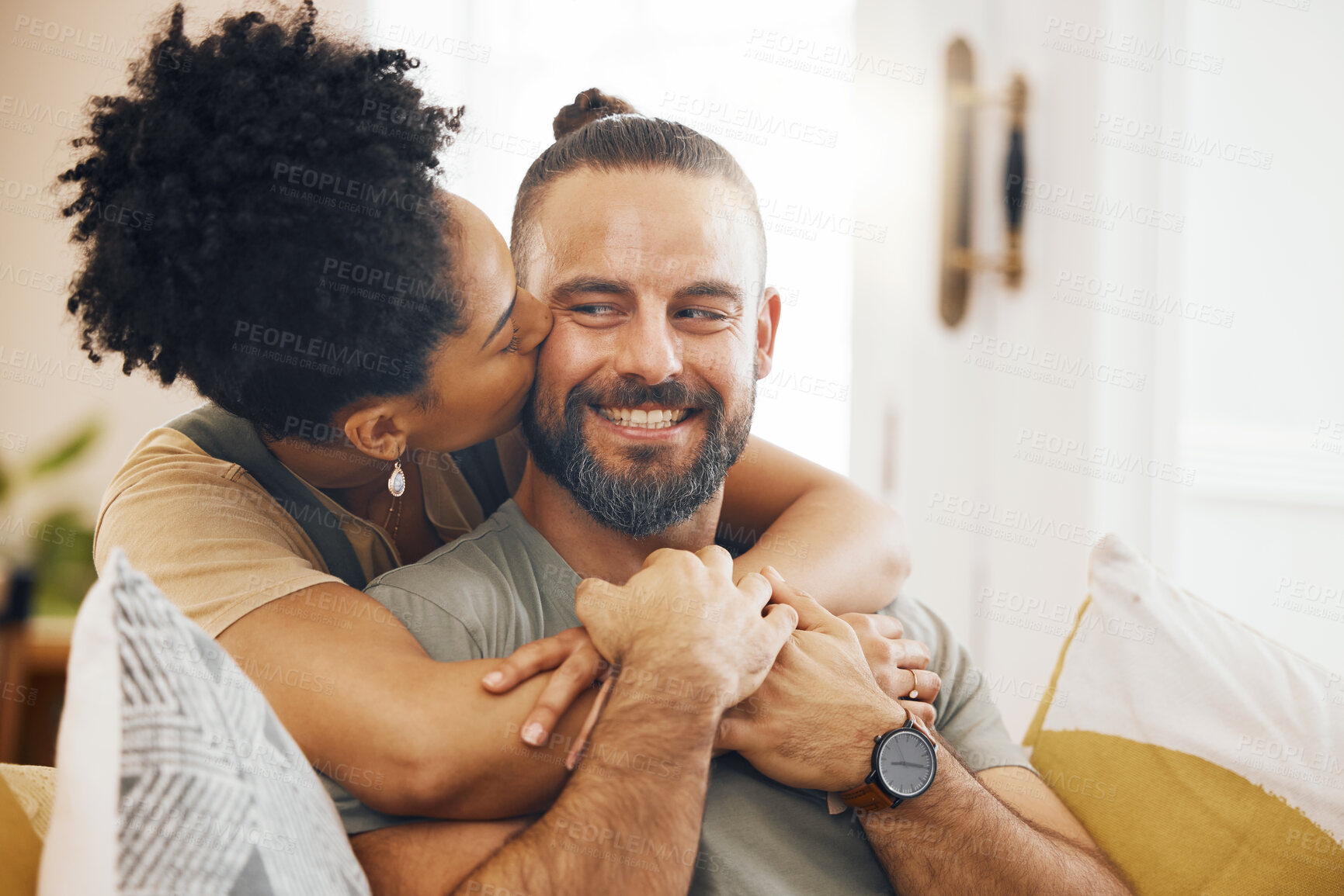 Buy stock photo Interracial couple, hug and kiss, happy on couch and relax at home with bonding, commitment and affection. Healthy relationship, marriage and love with care and trust, people in lounge with romance