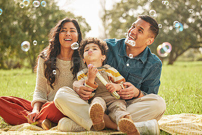 Buy stock photo Blowing bubbles, family portrait and happy at park, bonding and having fun together outdoor. Soap toy, child and parents at garden, mother and father smile on picnic blanket, care and play in nature