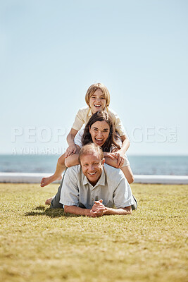 Buy stock photo Portrait, grass and family in a pile by the ocean together for travel, vacation or holiday on a summer morning. Love, smile or happy with a father, mother and son on the ground in a stack at the sea