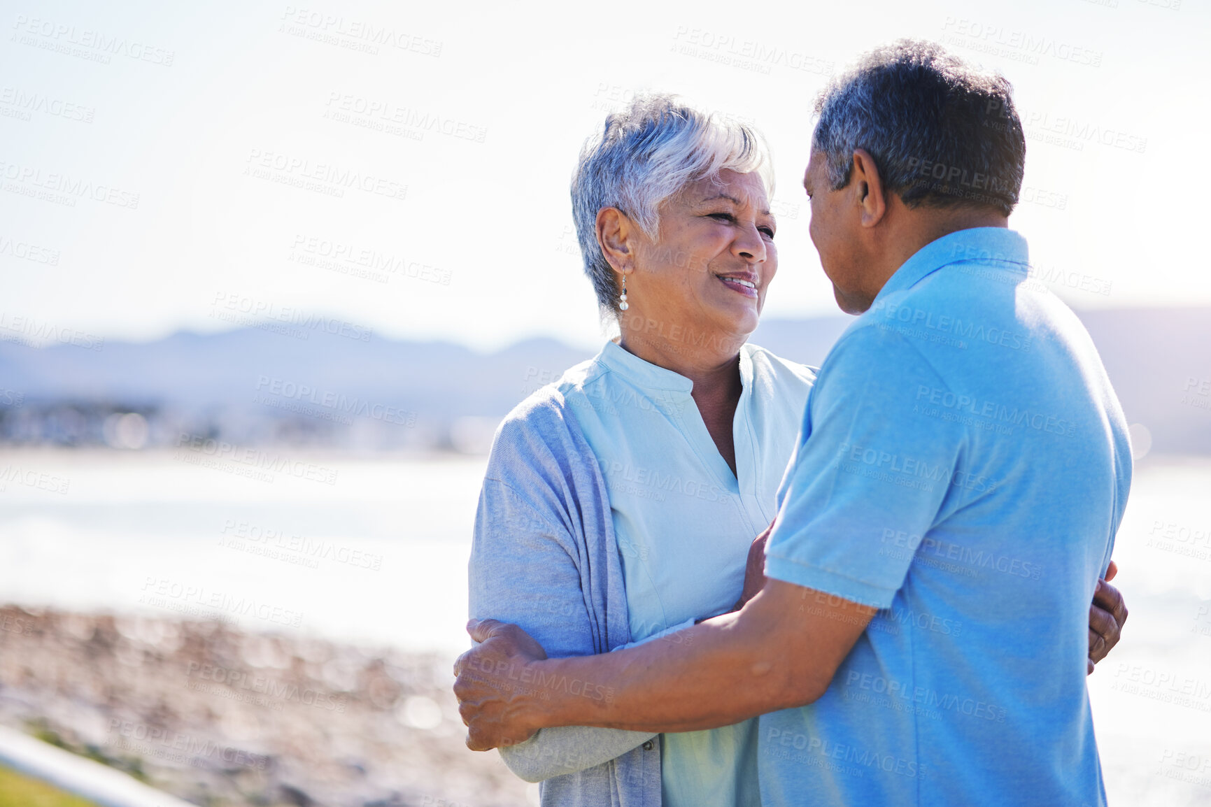 Buy stock photo Happy, love and senior couple at a beach with conversation, romance and bond with a smile on relax holiday. Marriage, retirement and old woman embrace elderly man at sea with trust, care and support