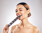 Skincare, diet and happy woman in studio with dark chocolate for anti aging benefits on white background. Sugar, beauty and lady model face, smile and eat candy bar for collagen, diet or pigmentation