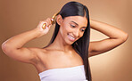 Beauty, smile and woman brushing hair in studio for growth, texture or shine against a brown background space. Haircare, cosmetics and female wellness model with brush, tool or hairstyle satisfaction