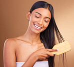 Smile, hair care and woman with a brush, glow and natural beauty on a brown studio background. Person, girl or model with style, luxury or shampoo with texture, comb or cosmetics with shine or volume