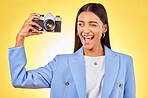 Camera, photography and woman picture with a smile and wink for job in studio. Happy, young female person and yellow background with creative, memory and funny emoji face with photographer skill
