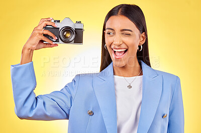 Buy stock photo Camera, photography and woman picture with a smile and wink for job in studio. Happy, young female person and yellow background with creative, memory and funny emoji face with photographer skill
