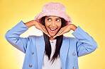 Fashion, happy and face of Indian woman on yellow background with silly, goofy and playful expression. Emoji, happiness and person in studio pose with hands in trendy accessories, style and cool hat