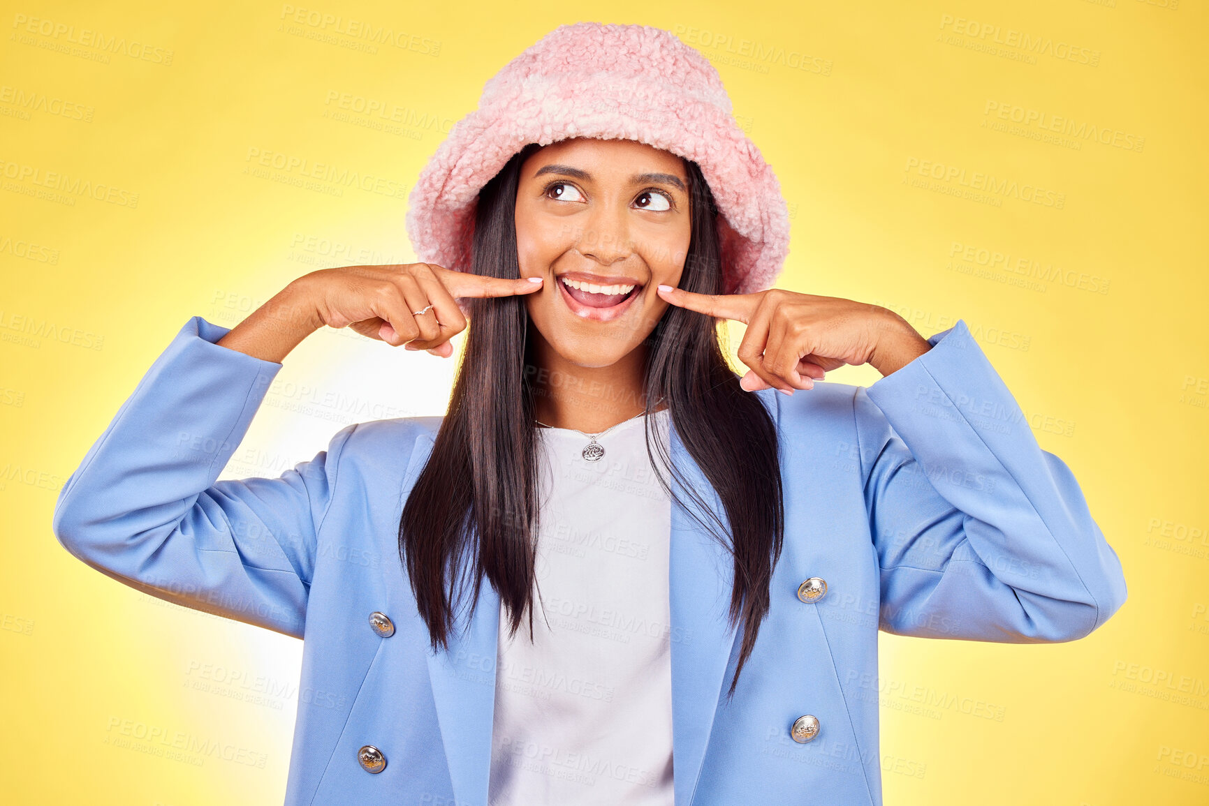 Buy stock photo Fashion, smile and face of Indian woman on yellow background with silly, goofy and playful expression. Emoji, happiness and person in studio pointing to mouth in trendy accessories, style and hat