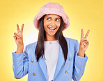 Fashion, peace sign and face of Indian woman on yellow background with smile, positive attitude and happy. Emoji, smile and person in studio with hand gesture in trendy accessories, style and hat