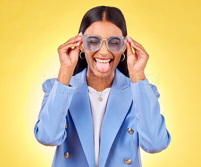 Buy stock photo Funny, woman smile and sunglasses with tongue out, comedy and silly face in a studio. Yellow background, crazy and female person with modern fashion, trendy cool style and creative work clothing