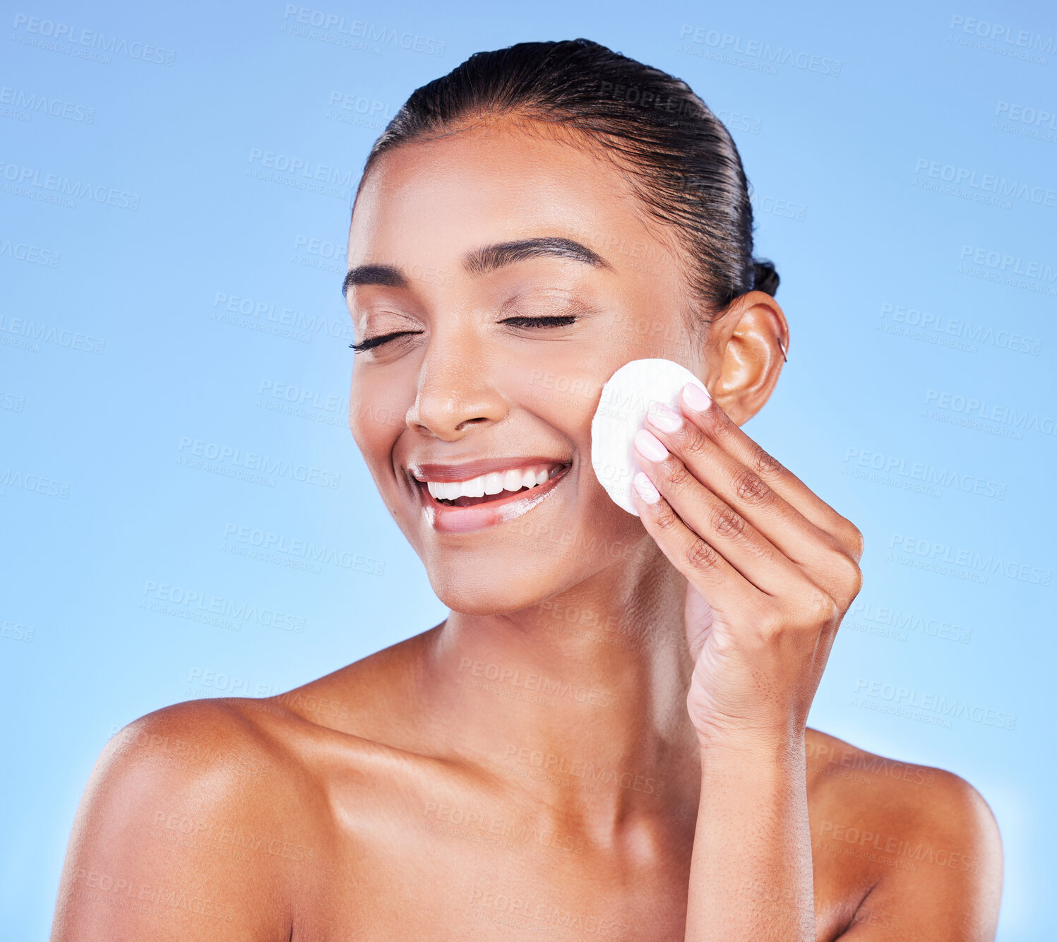 Buy stock photo Woman, face and cotton pad for skincare, cosmetics and aesthetic shine on blue background in studio. Happy indian model, facial cleaning and eyes closed for beauty of dermatology, glow or wipe makeup