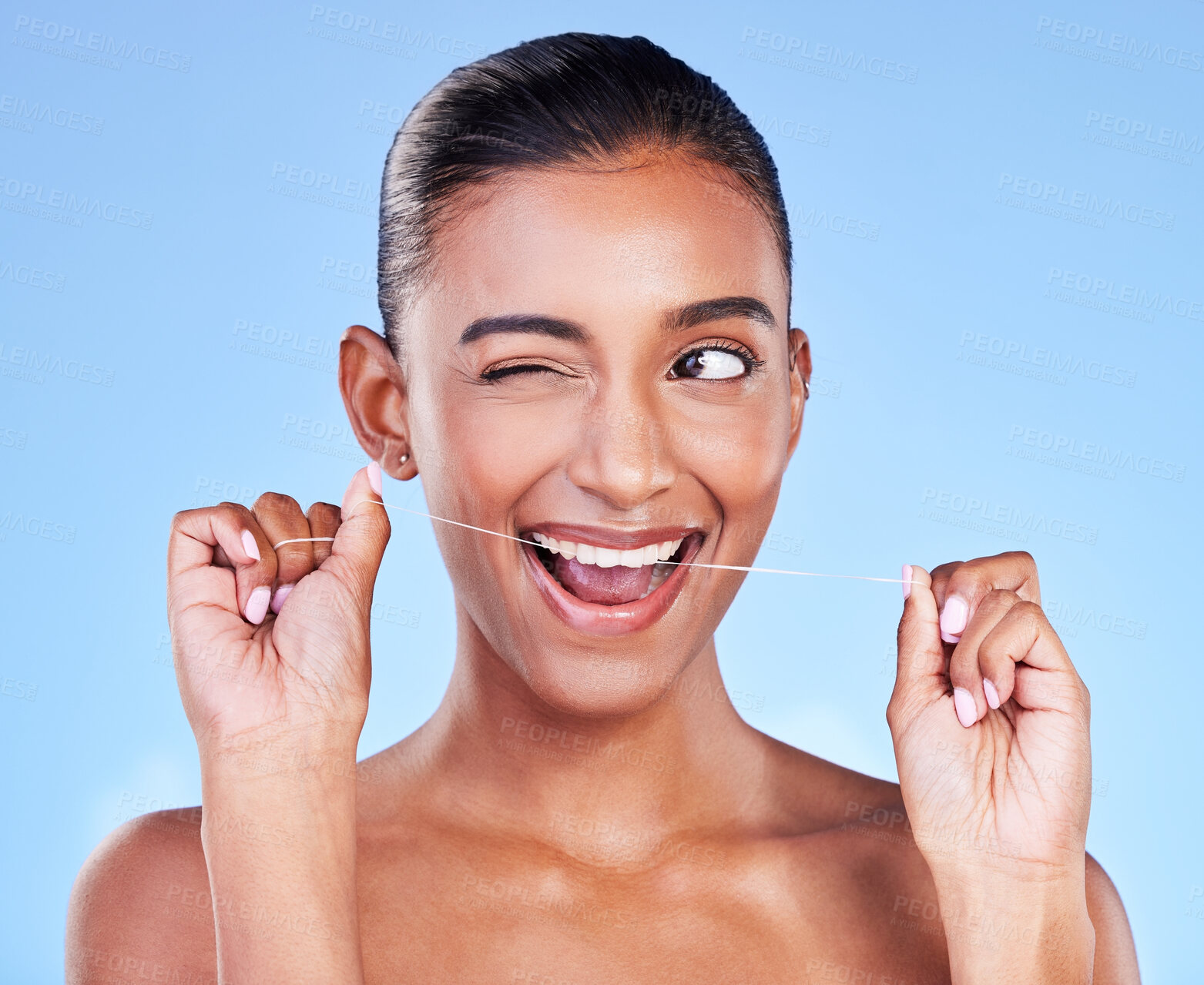 Buy stock photo Woman, wink and floss teeth in studio for healthy dental care, gum gingivitis and plaque on blue background. Face of happy indian model cleaning mouth with oral thread, fresh breath and tooth hygiene