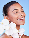 Skincare, flower and happy woman in studio for beauty, wellness and organic body care on blue background. Floral, face and Indian female model smile with orchid for eco friendly dermatology or shine