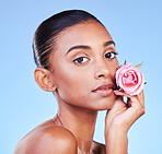 Rose, portrait and skincare of woman on blue background for eco cosmetics, natural glow and aesthetic in studio. Face, indian model and flowers for vegan beauty, sustainability or floral dermatology 