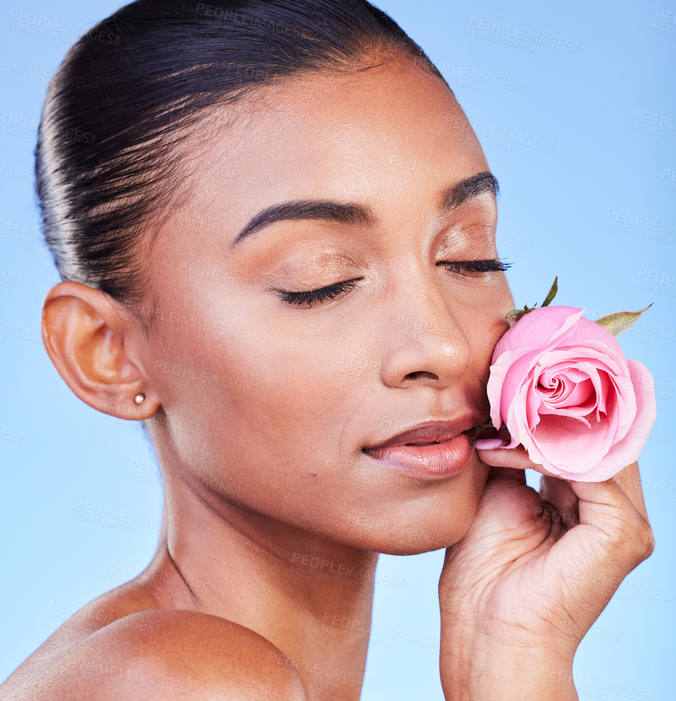 Buy stock photo Rose, face and skincare of woman in studio for eco cosmetics, natural wellness or blue background. Indian model, flowers and eyes closed for vegan beauty, sustainable dermatology and floral aesthetic