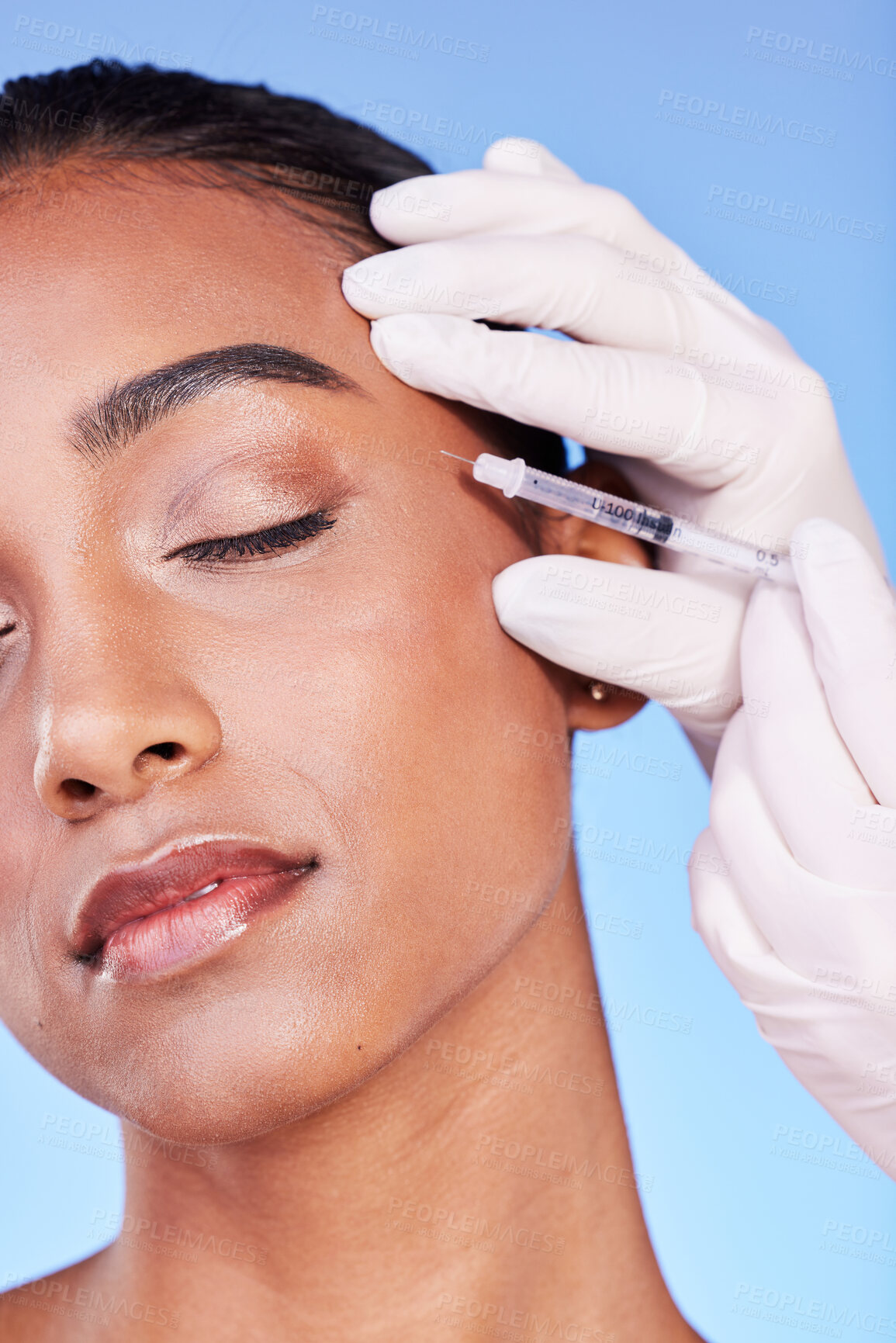 Buy stock photo Needle, woman and face on blue background for beauty, skincare process and aesthetic filler in studio. Indian model, hands of surgeon and injection for plastic surgery, facial change or prp cosmetics