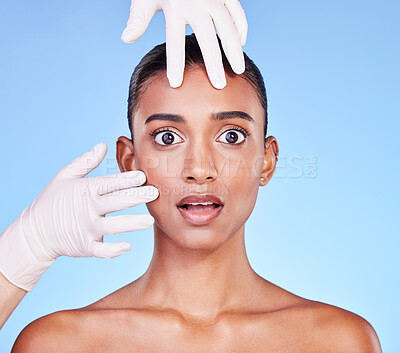 Scared, doctor and portrait of Indian woman for plastic surgery, cosmetics and skincare in studio. Dermatology, shock and hands on face of person for anti aging, botox and beauty on blue background