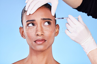 Injection, hands and face of Indian woman for plastic surgery, cosmetics and skincare in studio. Dermatology needle, anxiety and surgeon and person for anti aging, botox and beauty on blue background