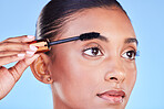 Woman, face and mascara in beauty makeup, cosmetics or eye brush against a blue studio background. Closeup of female person applying eyeshadow on eyelashes for volume, product or facial treatment