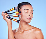 Woman, makeup and face brush in studio for beauty, cosmetics and aesthetic tools on blue background. Indian model, facial dermatology and eyes closed with set of skincare products for transformation