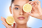 Woman, portrait and lemon on eyes in studio for vitamin c cosmetics, eco friendly beauty or detox diet. Face of model, healthy skincare or citrus fruits for sustainable dermatology on blue background