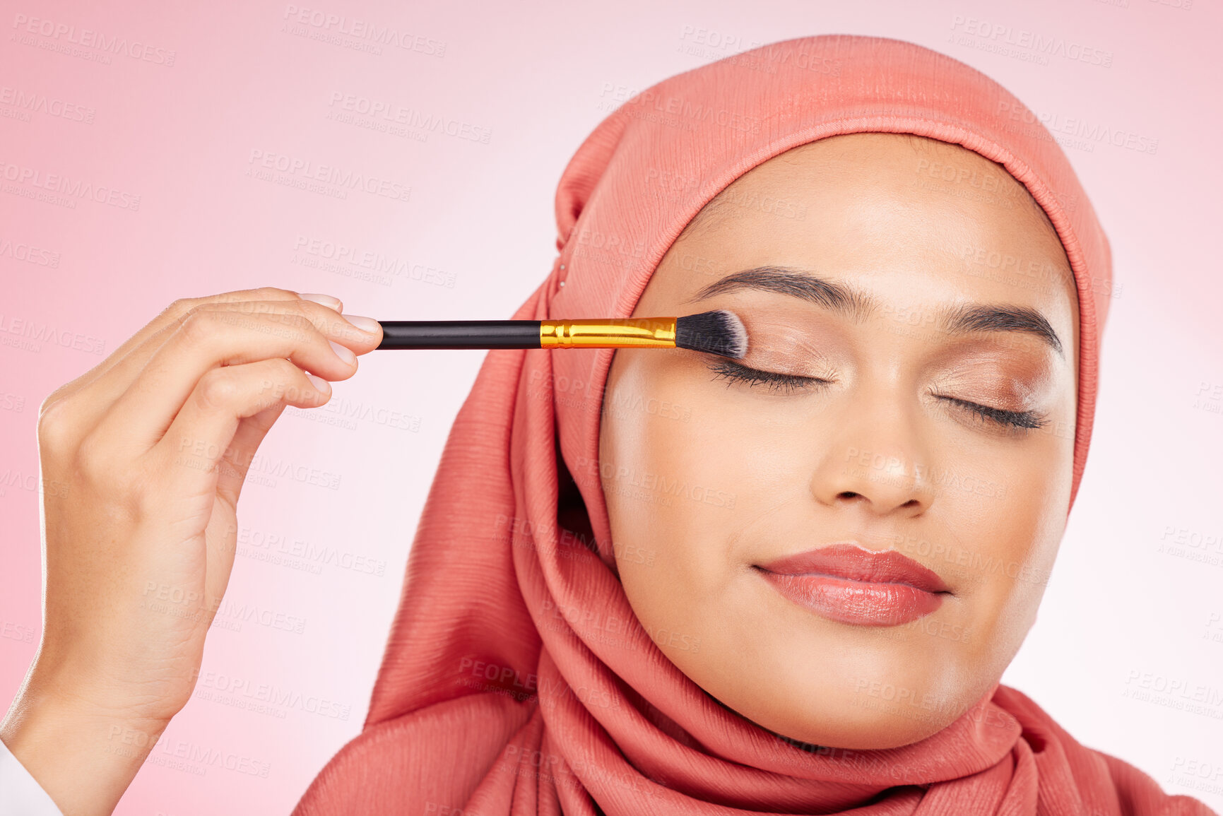 Buy stock photo Beauty, makeup and muslim woman in studio with a brush for eyeshadow, glamour or face routine. Cosmetics, self care and young islamic female model with cosmetology product isolated by pink background