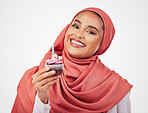 Portrait, candle in a cupcake and an islamic woman in studio on white background for dessert. Face, smile and food with a happy young muslim person eating a cake, candy or sugar snack in celebration