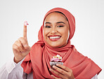 Portrait, cupcake and icing on finger with a muslim woman in studio on a white background for dessert. Face, smile and food with a happy young islamic person eating a cake, candy or sugar snack