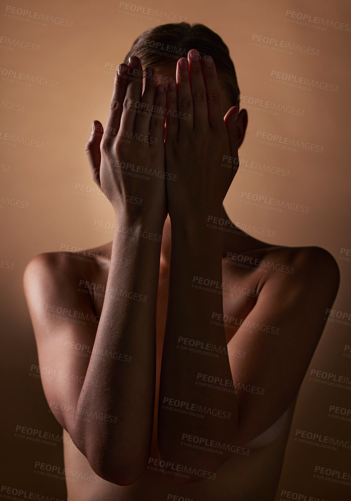 Buy stock photo Woman, body and hands covering face on dark brown background in studio for creative aesthetic, art deco and skin texture. Shy person, model and hide in shadow for nude beauty, wellness and sensuality