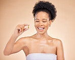 Skincare, smile of black woman and fish oil for beauty isolated on a brown background in studio. Happy, natural cosmetics and omega 3 supplements, biotin or vitamin pills of African model for health