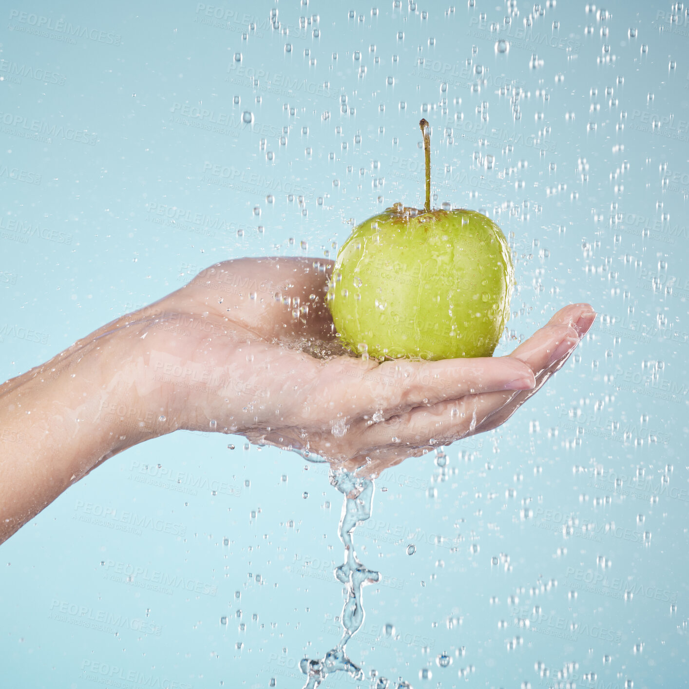 Buy stock photo Person, hands and apple in water drops for diet, healthy wellness or eating plan against a blue studio background. Closeup of model holding natural organic green fruit in shower, health or nutrition