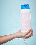 Person, hand and shower with shampoo product in hygiene, washing or cleanse against a blue studio background. Closeup of model holding hair cosmetics, soap or body care with water drops in bathroom
