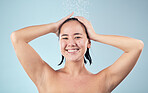 Face, shower and happy woman cleaning hair in studio isolated on a blue background. Water splash, hygiene and portrait of natural Asian model smile, washing and bathing for wellness, beauty and care
