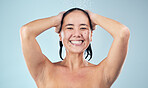 Face, shower and happy woman washing hair in studio isolated on blue background. Water splash, hygiene and portrait of natural Asian model smile, cleaning or bathing for wellness, beauty and cosmetic