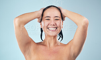 Buy stock photo Face, shower and happy woman washing hair in studio isolated on blue background. Water splash, hygiene and portrait of natural Asian model smile, cleaning or bathing for wellness, beauty and cosmetic
