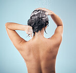 Hair shampoo, shower and back of woman cleaning in studio isolated on a blue background. Water splash, hygiene and soap, foam or cosmetics of model washing, bath or wellness for body care in bathroom