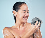 Woman, shower and clean with water, soap and sponge for healthy dermatology, skincare and blue background in studio. Person, smile and washing skin, body and self care with cosmetics in bathroom