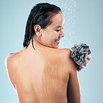 Happy woman, shower and back in water drops with loofah in hygiene, grooming or washing against a blue studio background. Rear view of female person in body wash, cleaning or wet skincare in bathroom
