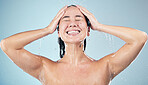 Happy woman, shower and water drops in hygiene, washing or grooming against a blue studio background. Female person smile in relax body wash, cleaning or skincare routine under rain in bathroom