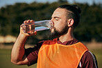 Sports, drinking water and man in field to rest after training, workout and exercise outdoors. Fitness, health and male athlete with liquid bottle for wellness, nutrition and hydration for practice