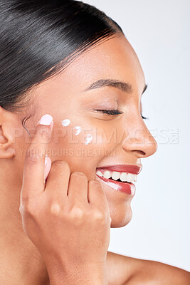 Buy stock photo Smile, skincare and a woman with cream on a white background for beauty, wellness or cosmetics. Happy, collagen and side of an Indian person or model with lotion or sunscreen for a facial treatment