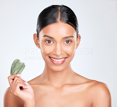 Buy stock photo Portrait, beauty and gua sha face massage with a woman in studio on a white background holding a stone. Smile, skincare and facial with a happy young model looking confident at luxury wellness