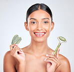 Portrait, beauty and gua sha facial massage with a woman in studio on a white background holding a stone. Smile, skincare and face roller with a happy young model looking confident at luxury wellness