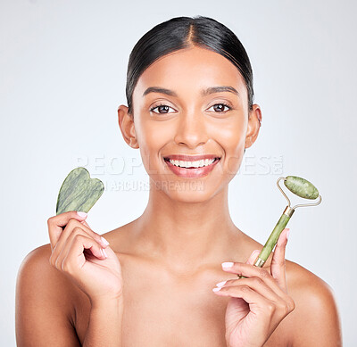 Buy stock photo Portrait, beauty and gua sha facial massage with a woman in studio on a white background holding a stone. Smile, skincare and face roller with a happy young model looking confident at luxury wellness