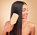 Hair care, brush and young woman in a studio with salon keratin treatment for wellness and self care. Grooming, cosmetic and Indian female model with tool for hairstyle isolated by a brown background