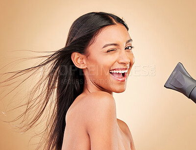 Buy stock photo Wink, hair and portrait of happy woman with hairdryer for beauty isolated in a studio brown background with strong texture. Aesthetic, glow and young person with heat or wind for health and shine
