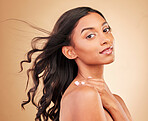 Curly hair, face and woman in wind at studio isolated on a brown background. Hairstyle breeze, natural cosmetics and portrait of Indian model in salon treatment for beauty, hairdresser and balayage